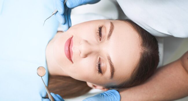Relaxed woman is visiting dentist stock photo Young female is lying in dental chair while doctor is doing check up with tools