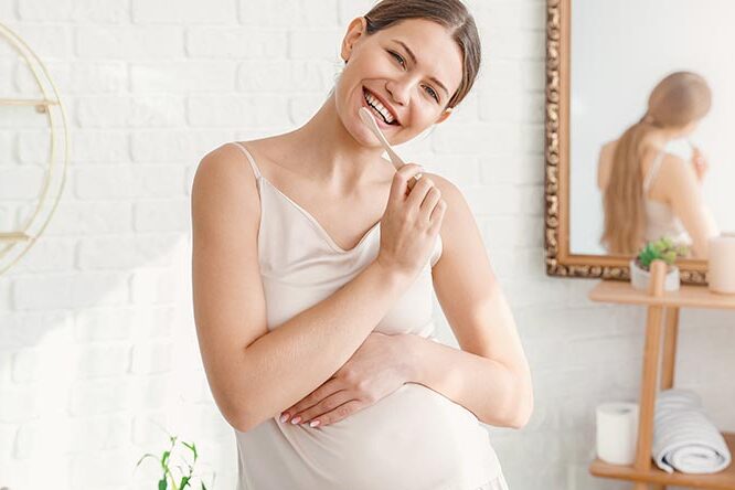 Young pregnant woman brushing teeth in bathroom